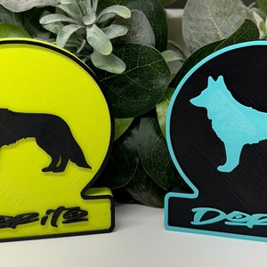 Può includere: Due figurine di silhouette di cane stampate in 3D con la parola "Derito" stampata sulla base. Una figurina è nera su una base gialla e l'altra è blu su una base nera.