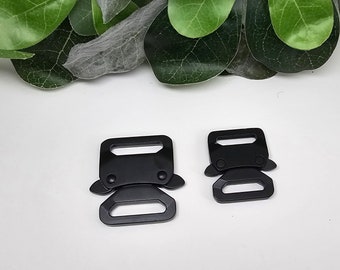 May include: Two black metal side release buckles. The larger buckle is approximately 5 cm long and the smaller buckle is approximately 4 cm long.