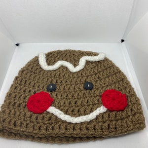 May include: Brown crocheted gingerbread man hat with white icing and red buttons for cheeks.