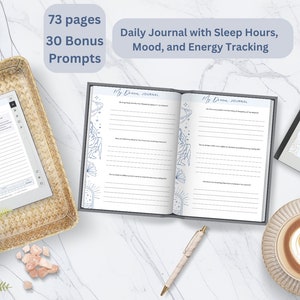 Könnte beinhalten: Ein offenes Journal mit linierten Seiten und dem Text "My Dream Journal" wird neben einem geschlossenen Journal und einem E-Reader angezeigt. Das Bild zeigt auch eine Tasse Kaffee, einen Stift und dekorative Pflanzen. Der Text auf dem Bild lautet "73 Seiten, 30 Bonus Prompts, Daily Journal with Sleep Hours, Mood, and Energy Tracking."