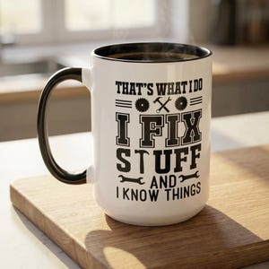May include: A white ceramic mug with a black interior and handle, featuring black text that reads: THAT'S WHAT I DO I FIX STUFF AND I KNOW THINGS, accompanied by graphic icons of circular saw blades, a hammer, and crossed wrenches.