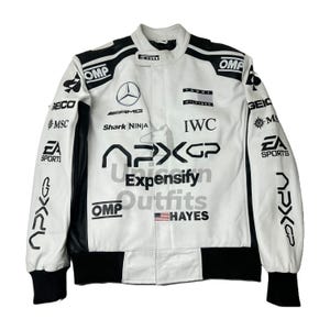 Op de afbeelding: Witte racejas met zwarte accenten, met sponsorlogo's en tekst. De jas heeft een opstaande kraag, zwarte manchetten en een zwarte zoom. Logo's zijn onder meer "OMP", "AMG", "IWC" en "EA SPORTS".