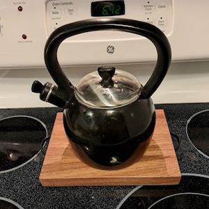 May include: A black kettle with a silver lid sits on a wooden cutting board on a black stovetop. The stovetop has a digital timer that reads "6:42".