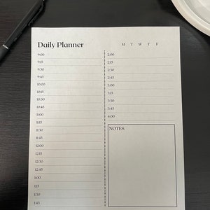 May include: A white daily planner with a black and white grid for scheduling appointments and notes. The planner has a section for each day of the week, Monday through Friday, and a notes section.