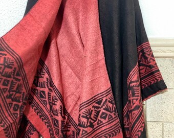 May include: Reversible black and red shawl with geometric patterns. The shawl features a black exterior and a red interior, with black geometric designs along the edges. The shawl has a fringed hem.