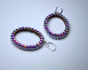 May include: A pair of iridescent crystal hoop earrings with silver hooks. The hoops are made of a thin metal band covered in small, faceted crystals.