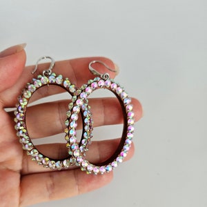 May include: A pair of large oval hoop earrings with a silver hook and a border of iridescent rhinestones.