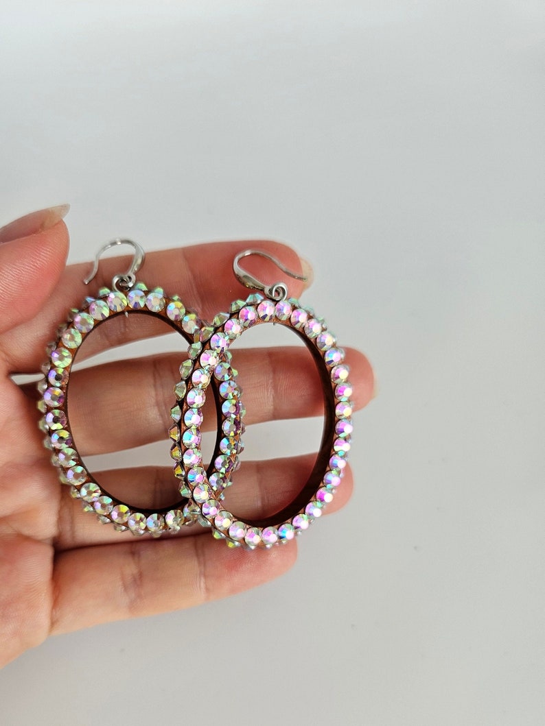 May include: A pair of large oval hoop earrings with a silver hook and a border of iridescent rhinestones.