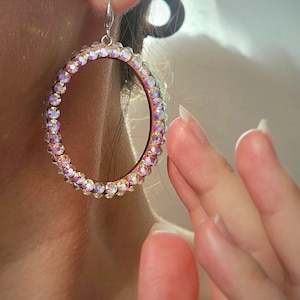 May include: A pair of large, oval-shaped earrings with a silver-toned metal setting. The earrings are adorned with iridescent rhinestones that create a sparkling effect.