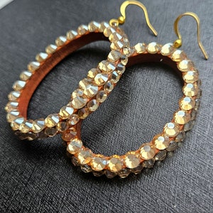 May include: A pair of large hoop earrings with gold hooks. The hoops are covered in clear rhinestones.