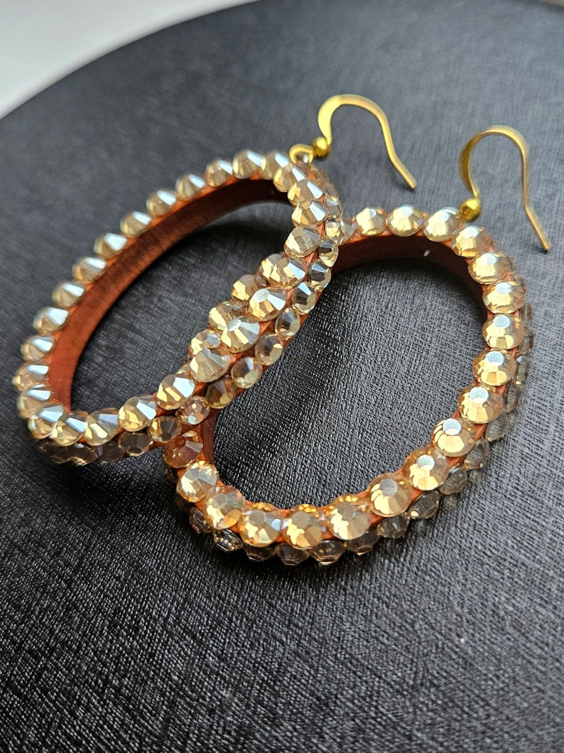 May include: A pair of large hoop earrings with gold hooks. The hoops are covered in clear rhinestones.