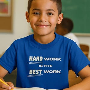 Può includere: Una t-shirt a maniche corte color blu reale con la scritta bianca "HARD WORK IS THE BEST WORK" stampata sul petto, con linee bianche orizzontali che sottolineano le parole "HARD" e "BEST" in un carattere sans-serif chiaro e audace.