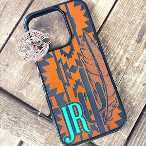 May include: A black phone case with an orange and black geometric pattern, a feather, and a cactus design. The initials "JR" are in turquoise. The case has a black border and the text "TEC LASER WESTERN LASER ENGRAVING".