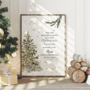 May include: A framed print featuring a watercolour Christmas tree and the text "MAY THE BEAUTIFUL LIGHTS OF EVERY Christmas Season REMIND US OF Him WHO IS THE SOURCE OF ALL LIGHT". The print is displayed near a decorated Christmas tree.