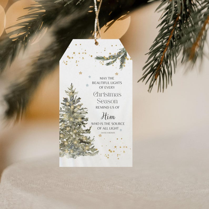 May include: A white Christmas gift tag featuring a watercolour illustration of a Christmas tree and the text "May the beautiful lights of every Christmas season remind us of Him who is the source of all light."
