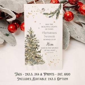 May include: A white Christmas gift tag featuring a Christmas tree illustration and the text "May the beautiful lights of every Christmas season remind us of Him". The tag is decorated with gold stars and a sprig of greenery.