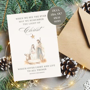 May include: A Christmas card with a watercolor illustration of the Nativity scene, including Mary, Joseph, and baby Jesus. The card has text that reads "When we see the star may we remember the light of Christ." The card is accompanied by a brown envelope.