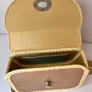 Puede incluir: Un peque&ntilde;o bolso de mano de cuero beige con ribete tejido y cierre de metal. El bolso tiene una solapa superior con un anillo de metal y un peque&ntilde;o bolsillo en el interior.