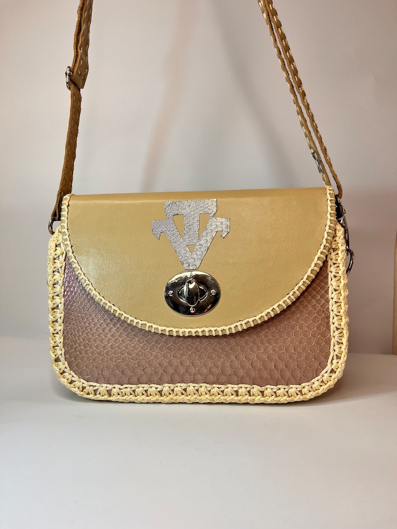 Puede incluir: Un bolso de cuero marr&oacute;n claro con cierre de plata y ribete de ganchillo. El bolso tiene un patr&oacute;n de piel de serpiente en la mitad inferior.