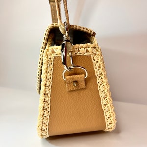 Puede incluir: Un bolso de mano de cuero marr&oacute;n con ribete de ganchillo. El bolso tiene un cierre plateado y una correa.