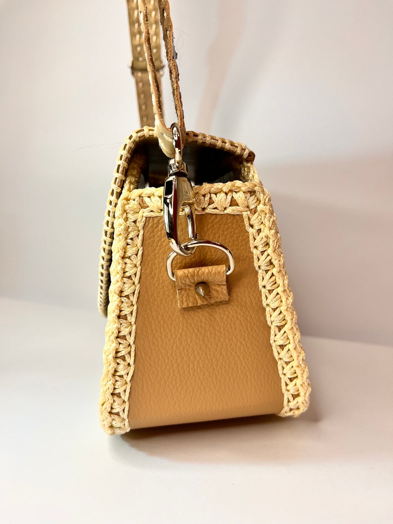 Puede incluir: Un bolso de mano de cuero marr&oacute;n con ribete de ganchillo. El bolso tiene un cierre plateado y una correa.