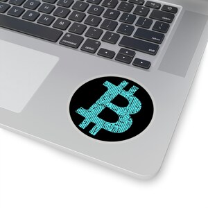 May include: A circular sticker featuring a bright cyan Bitcoin symbol filled with a detailed black circuit board pattern. The sticker is placed on the silver surface of a laptop, showcasing the contrast between the vibrant blue and black design.