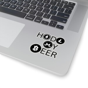 Puede incluir: Una pegatina de vinilo con el texto HODL MY BEER y logotipos de criptomonedas integrados en las letras. La O de HODL es un símbolo de Ethereum, la L es de Litecoin, la M es de Monero y la B de BEER es un símbolo de Bitcoin.