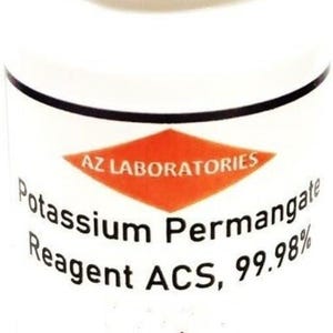 May include: A white cylindrical bottle with a white lid. The label features the text "AZ LABORATORIES" above "Potassium Permanganate Reagent ACS, 99.98%" and a hazard symbol. The bottle is for laboratory use.