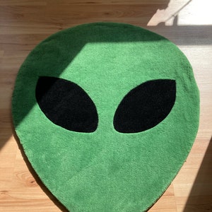May include: Green alien face rug with black eyes. The rug is made of a soft, plush material.