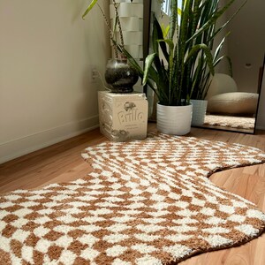 May include: A brown and white patterned rug with a wavy shape. The rug is made of a soft, fluffy material and has a geometric design.