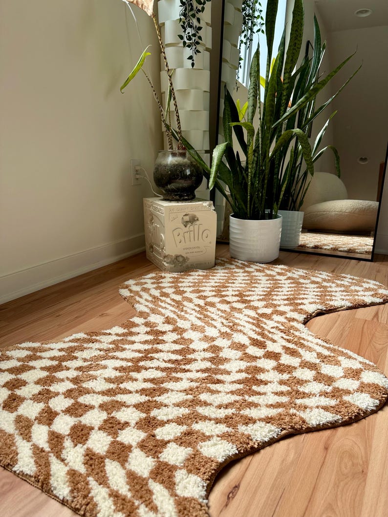 May include: A brown and white patterned rug with a wavy shape. The rug is made of a soft, fluffy material and has a geometric design.