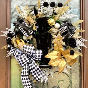 May include: A black and gold Christmas wreath with a black nutcracker, black and white checkered ribbon, gold poinsettias, and white and gold ornaments.