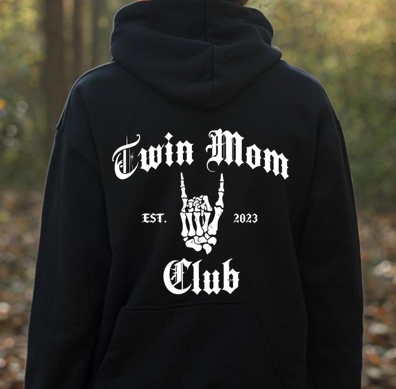 May include: Black hoodie with white text that reads "Twin Mom Club" with a skeleton hand making a rock and roll sign and the text "EST. 2023".