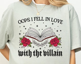 May include: A light green t-shirt with the text "Oops I fell in love with the villain" in black lettering. The text is surrounded by a black open book with red roses and stars.