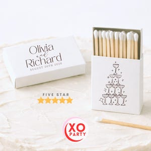 May include: White matchboxes with custom text "Olivia and Richard August 20th 2026". One box features a champagne glass tower design. The matches are natural wood with white tips. The image also includes a five-star rating.