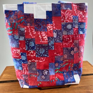 May include: A patchwork tote bag with red, blue, and white fabric squares. The bag has two handles and is made of a soft, quilted material.