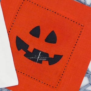 May include: Orange square fabric with a black Jack-o'-lantern face. The fabric has a stitched border and the text "JACK-O-LANTERN MINI FILL" at the top. The bottom of the image has the text "STITCHED BY @MAGNOLIAMADECUSTOM".