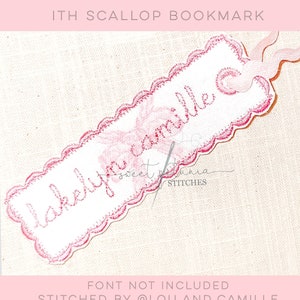 May include: A white bookmark with a scalloped edge and pink stitching. The bookmark has the text "la belle famille" written in pink cursive script.