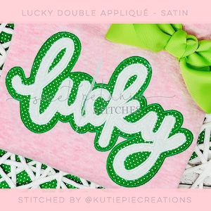 May include: A pink shirt with a green and white "lucky" applique. The applique has white polka dots on a green background. The shirt is on a white wicker surface.