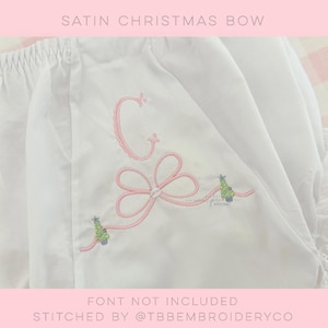 Peut inclure: Tissu blanc avec un nœud en ruban de satin rose et des sapins de Noël brodés. Le tissu a une lettre C brodée en point de satin rose. Le texte "FONT NOT INCLUDED" et "STITCHED BY @TBBEMBROIDERYCO" est en bas de l'image.