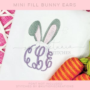 Peut inclure: Un tissu blanc avec une lettre 'C' brodée en violet et deux oreilles de lapin vertes et roses. Le texte 'FONT NOT INCLUDED' et 'STITCHED BY @KUTIEPIECREATIONS' est en bas de l'image.