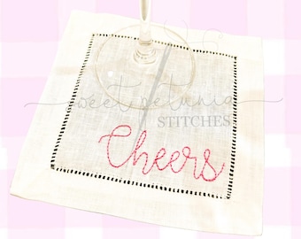 Könnte beinhalten: Weiße Cocktail-Serviette aus Leinen mit schwarzen Nähten an den Rändern. Die Serviette hat das Wort "Cheers" in rosa Garn gestickt.