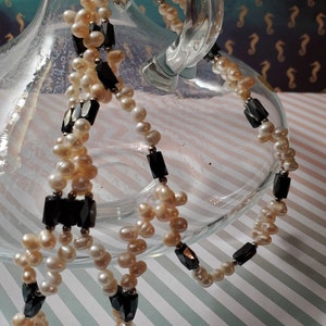 May include: A double strand necklace with white pearls and black faceted beads. The necklace is draped over a clear glass pitcher.
