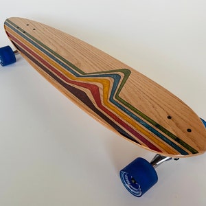 May include: A wooden longboard skateboard with blue wheels and a colorful rainbow design on the deck.