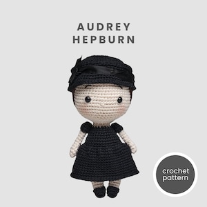 Może przedstawiać: Szydełkowa lalka Audrey Hepburn w czarnej sukience i kapeluszu z kokardą. Lalka ma jasną karnację, różowe policzki i czarne oczy. Tekst "AUDREY HEPBURN" znajduje się nad lalką, a "crochet pattern" w okręgu poniżej.