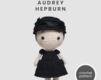 May include: A crocheted doll of Audrey Hepburn in a black dress and hat with a bow. The doll has a light skin tone, rosy cheeks, and black eyes. The text "AUDREY HEPBURN" is above the doll, and "crochet pattern" is in a circle below.