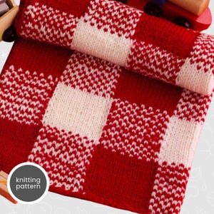 Może przedstawiać: Czerwono-biały pled dziany w kratkę. Pled jest złożony na pół, a wzór dziania jest widoczny.