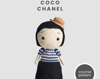 May include: Crochet pattern for a doll of Coco Chanel, wearing a black dress, a blue and white striped shirt, and a brown hat. The doll has black hair and a crocheted face.