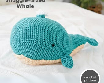 May include: A crocheted whale plush toy in teal blue with a white crocheted fin on top. The whale has a beige crocheted belly and black eyes. The toy is lying on a white surface with the text "crochet pattern" in a gray circle.