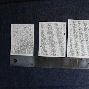 Pu&ograve; includere: Tre carte bianche con testo nero su uno sfondo di tessuto blu scuro. Le carte sono allineate orizzontalmente e misurano circa 5 cm di larghezza e 7,5 cm di altezza. Un righello &egrave; posizionato sotto le carte.
